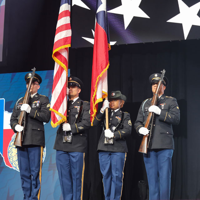 Four military personnel are standing and presenting the American flag and the Texas flag.